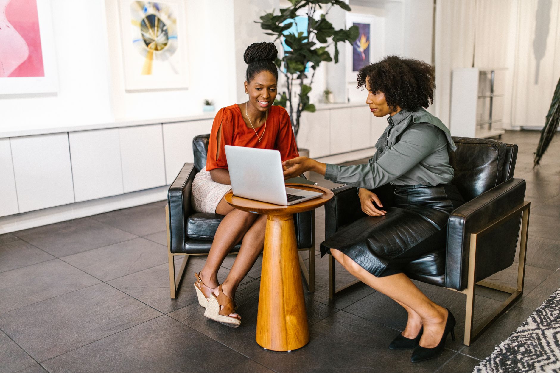 Two women collaborate on a project using a laptop in a stylish modern office setting.