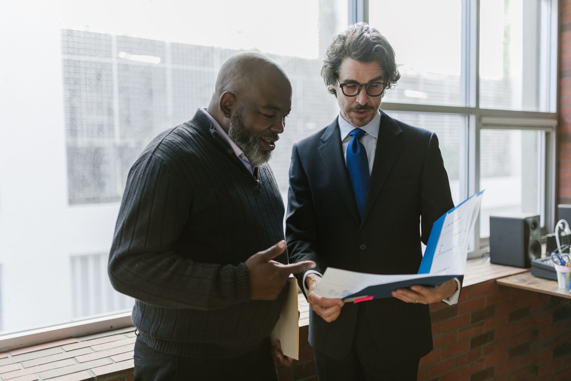Two businessmen discussing and reviewing documents in a modern office setting.