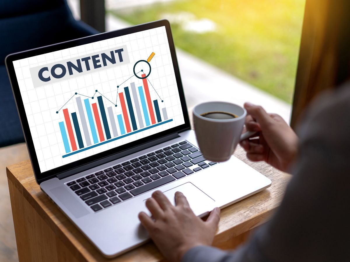 He/She holding a cup of coffee while touching the laptop with a word " Content"