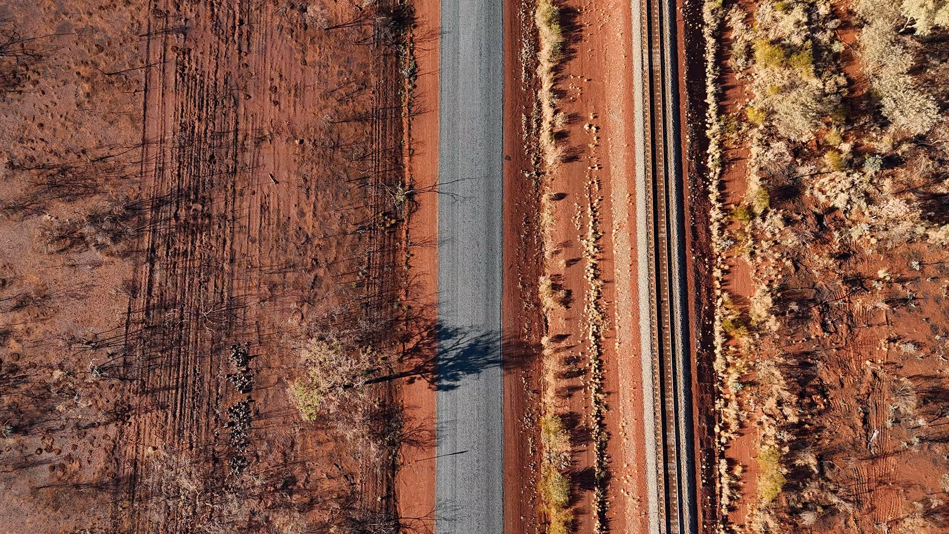Aerial view of a straight road and parallel railway track on red dirt terrain with sparse vegetation.