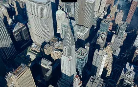Aerial view of a cityscape with tall skyscrapers casting long shadows in bright daylight.