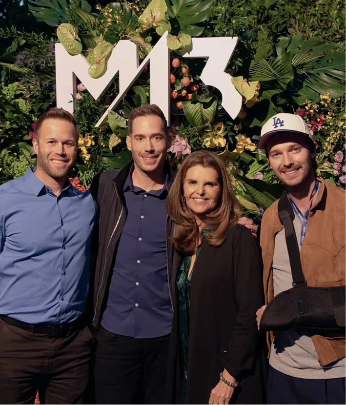 Four people standing closely in front of a green plant wall with a white M13 logo.