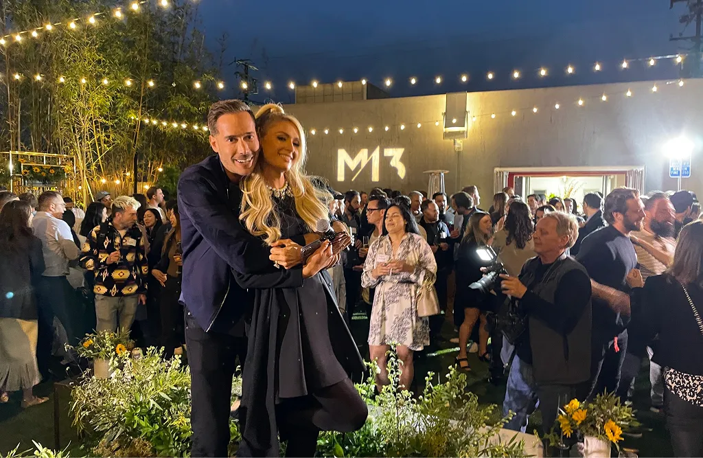 Couple hugging and smiling at an outdoor evening party with many guests and string lights overhead.