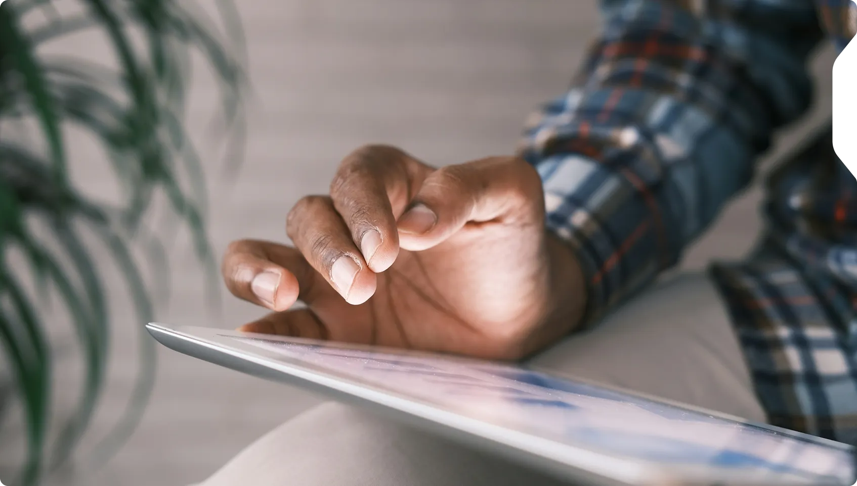 Person wearing a plaid shirt using a tablet device with their hand touching the screen.