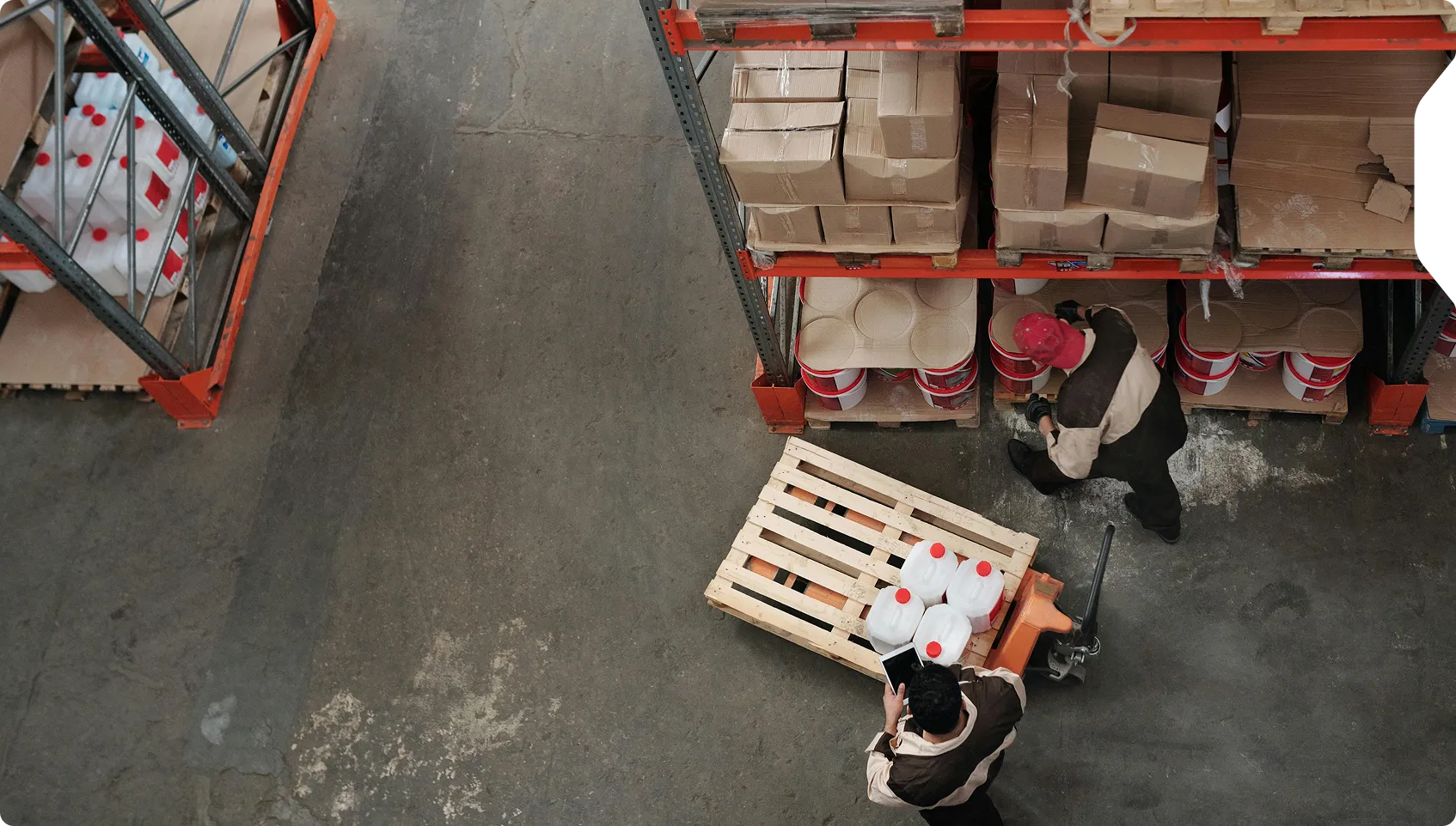 Two warehouse workers organizing shelves and checking inventory with a pallet jack and tablet.