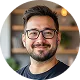 Smiling man with glasses and beard in a modern indoor setting.