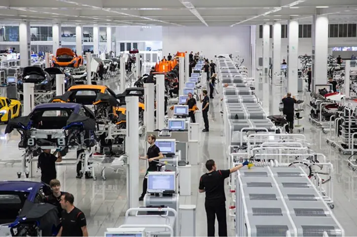 Modern car manufacturing assembly line with workers and partially assembled sports cars.