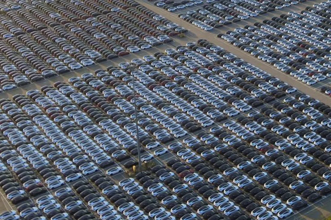 Aerial view of a large parking lot filled with hundreds of neatly lined cars.