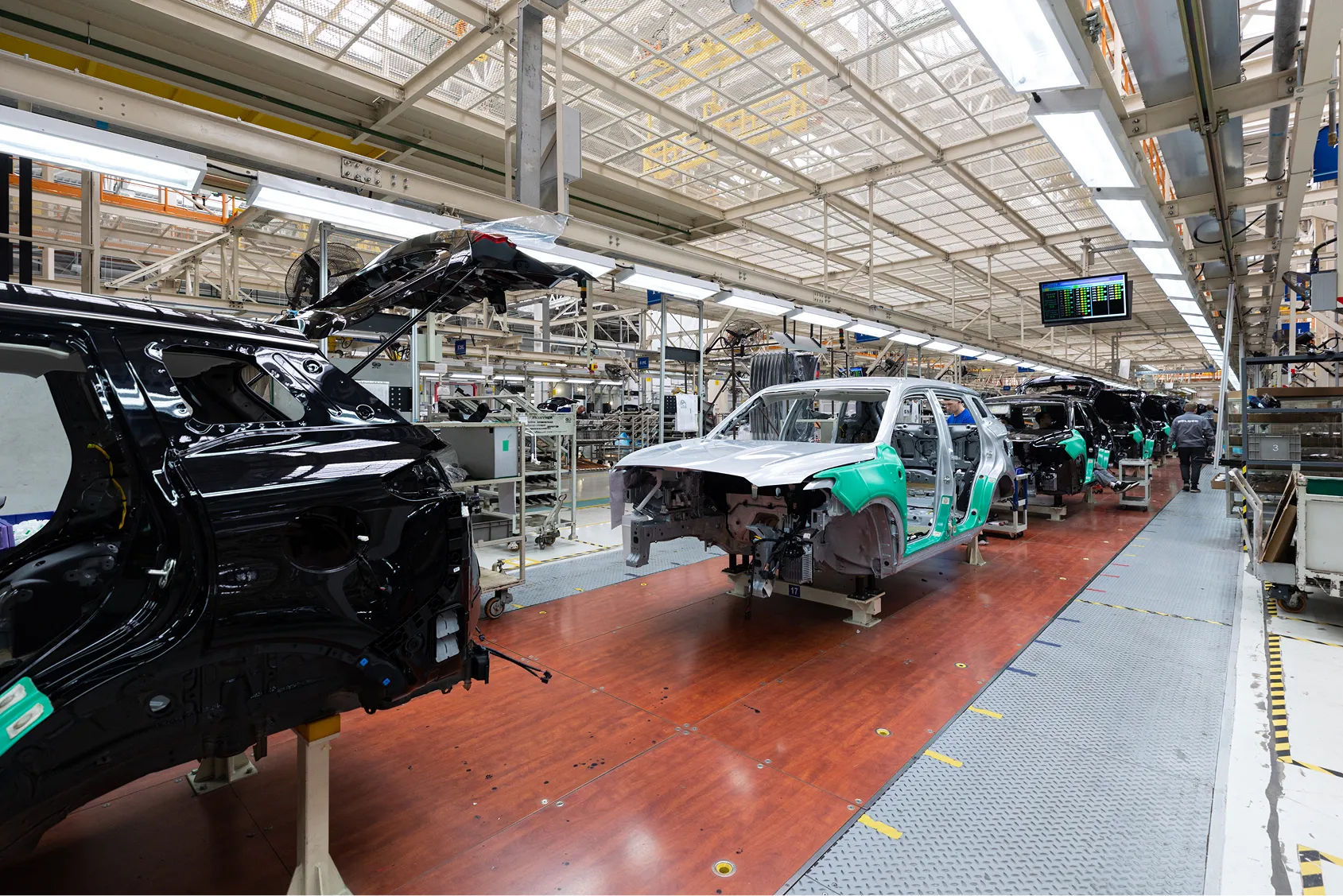 Car assembly line in a factory with several partially assembled vehicles on the production floor.