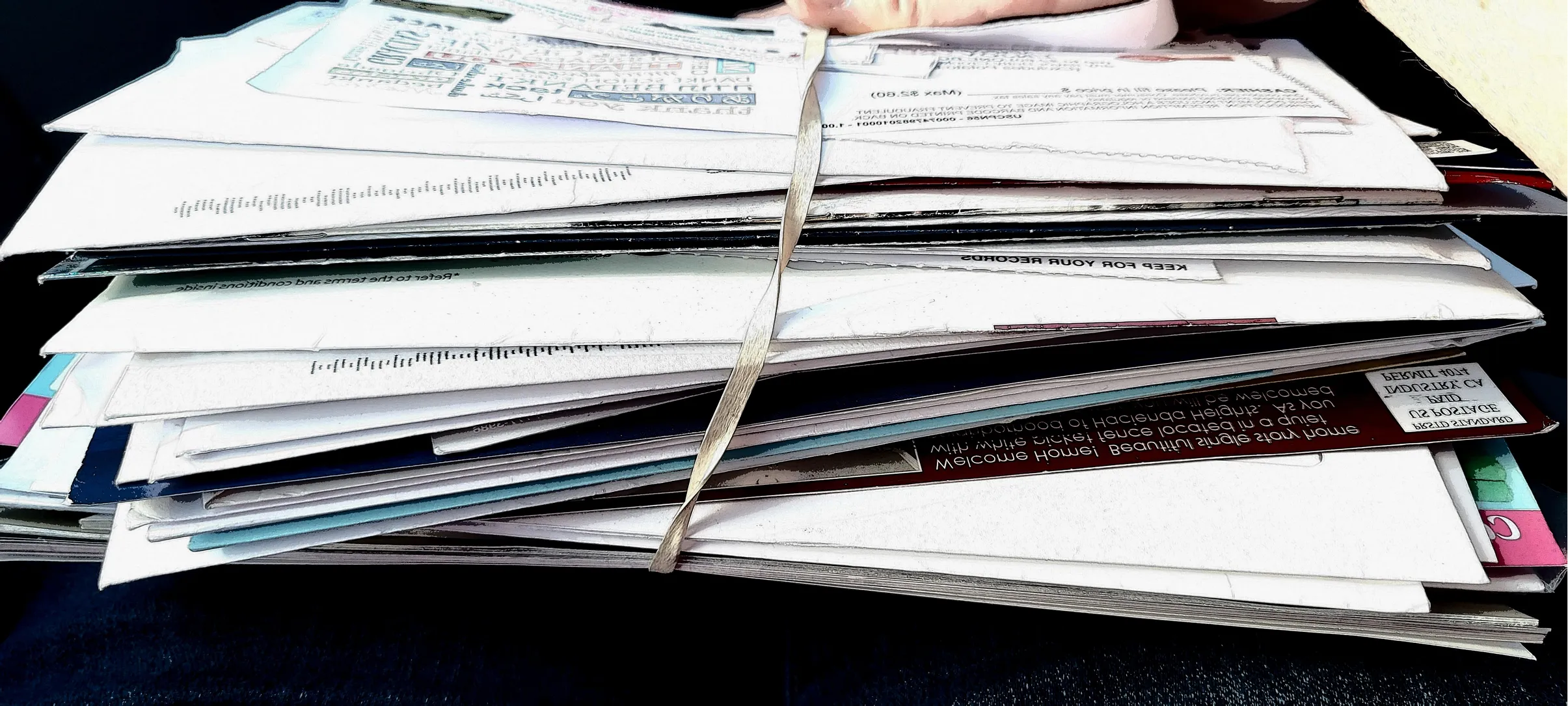 Stack of assorted envelopes and papers held together by a rubber band on a dark surface.