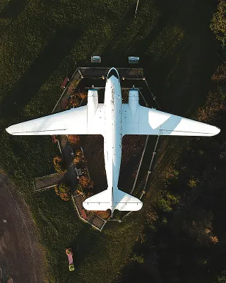 A white airplane viewed from directly above, parked on a grassy area surrounded by trees and pathways.