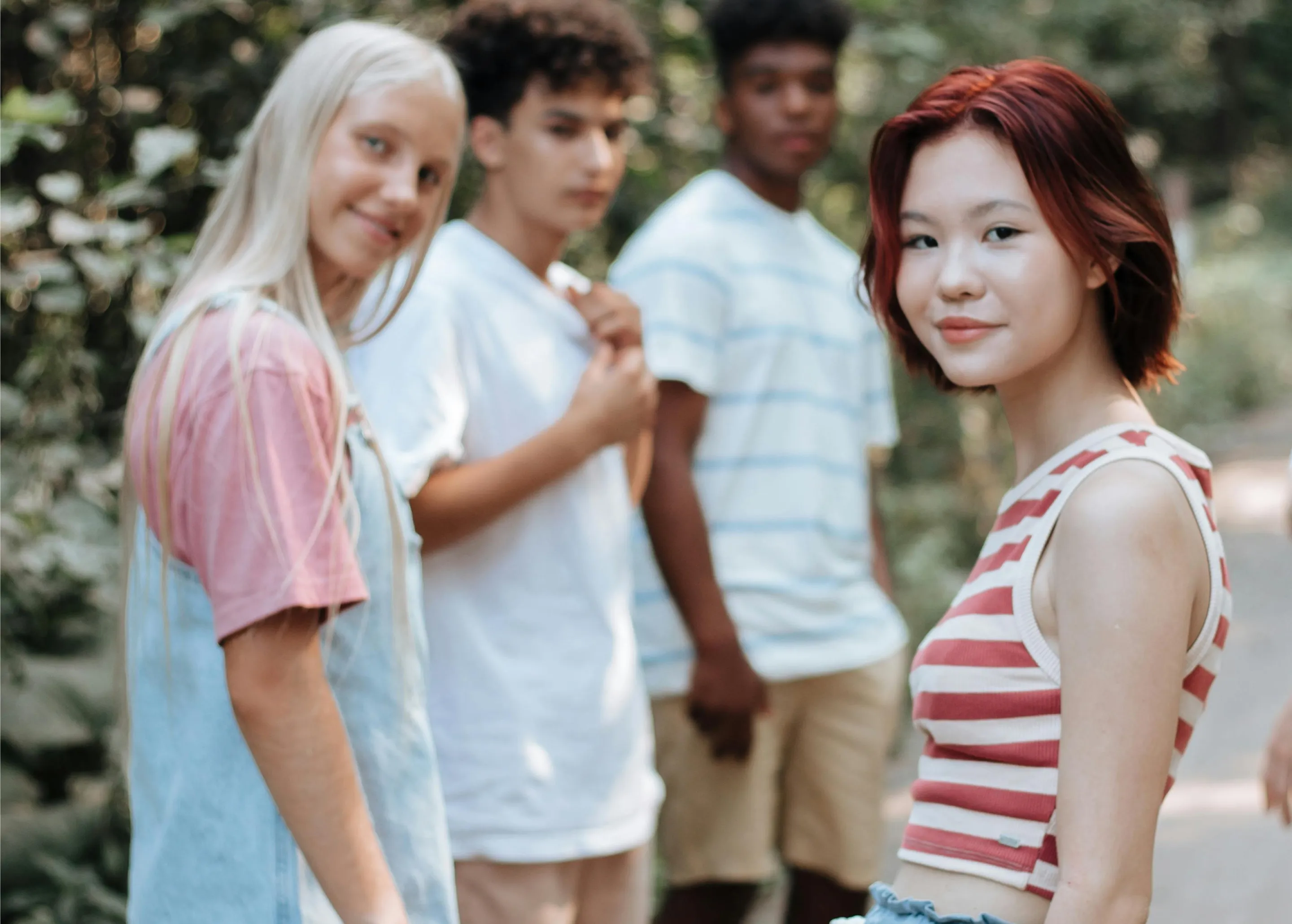 Group of four teenagers outdoors, with one girl in striped top facing the camera and smiling.