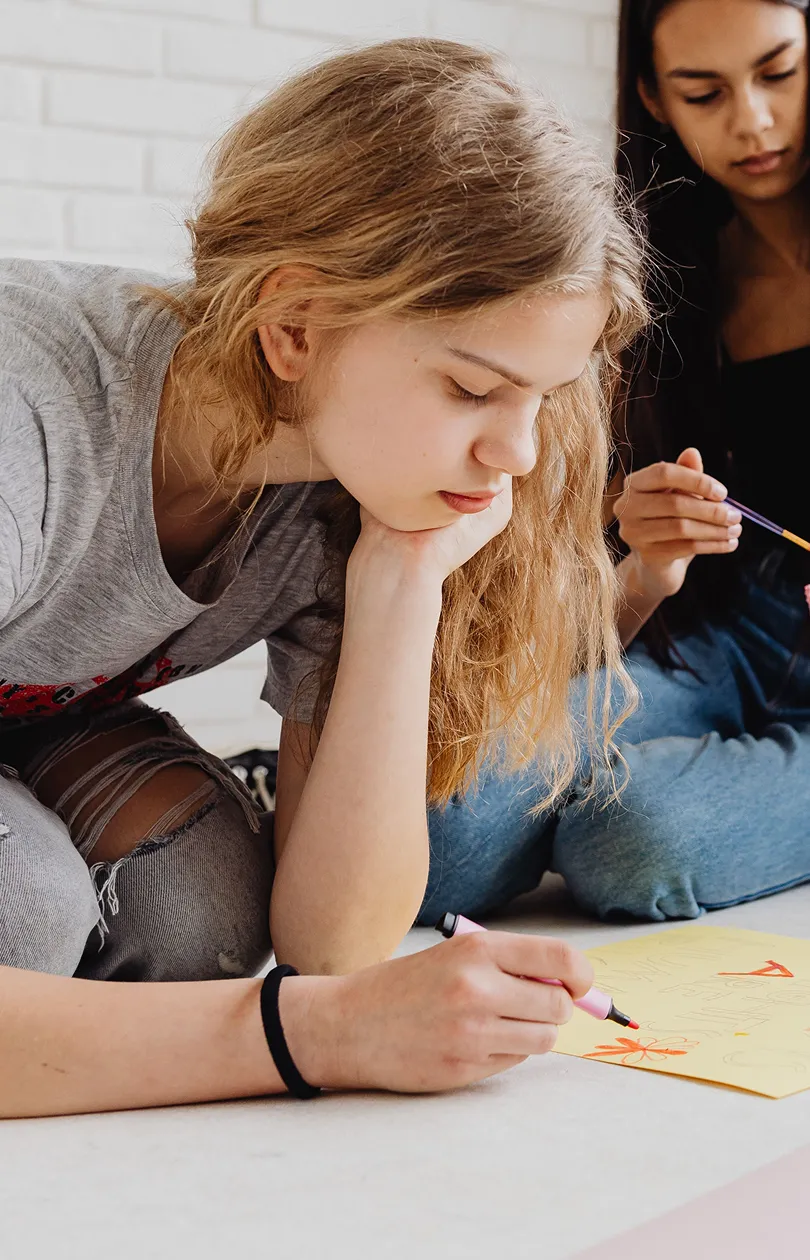 Two teenage girls drawing with markers on paper during a relaxed art activity.