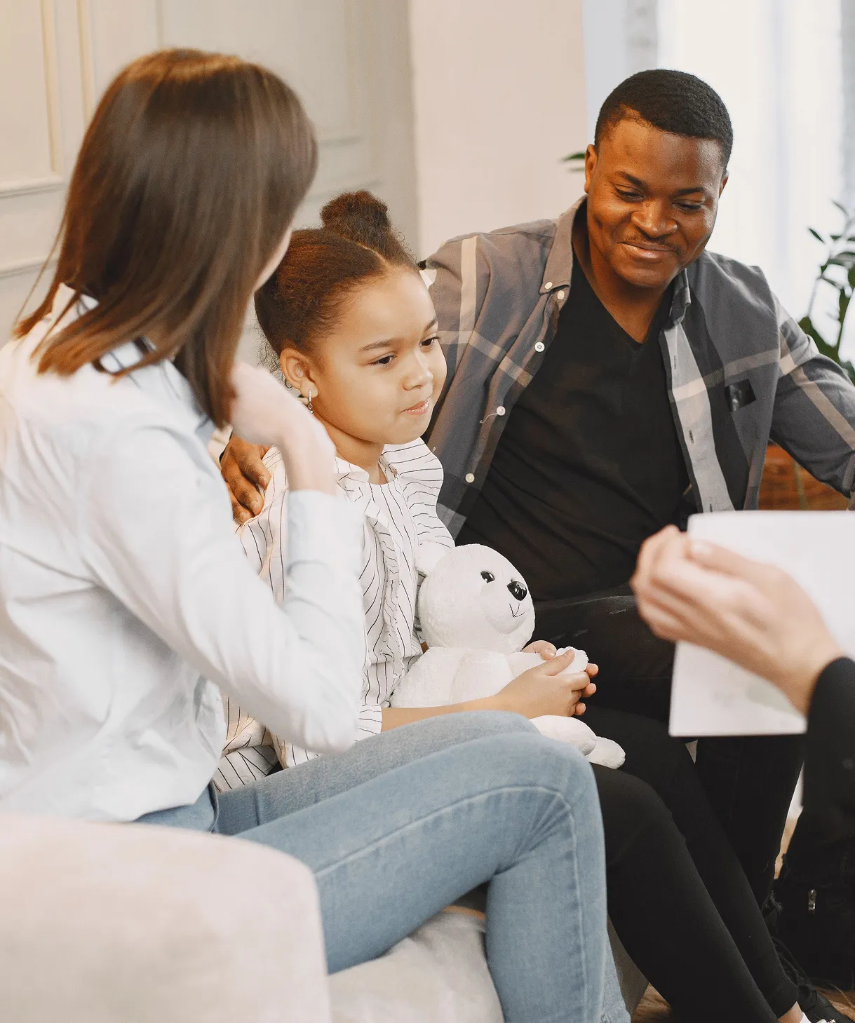 Young girl holding a stuffed animal between her parents during a family session with a therapist.