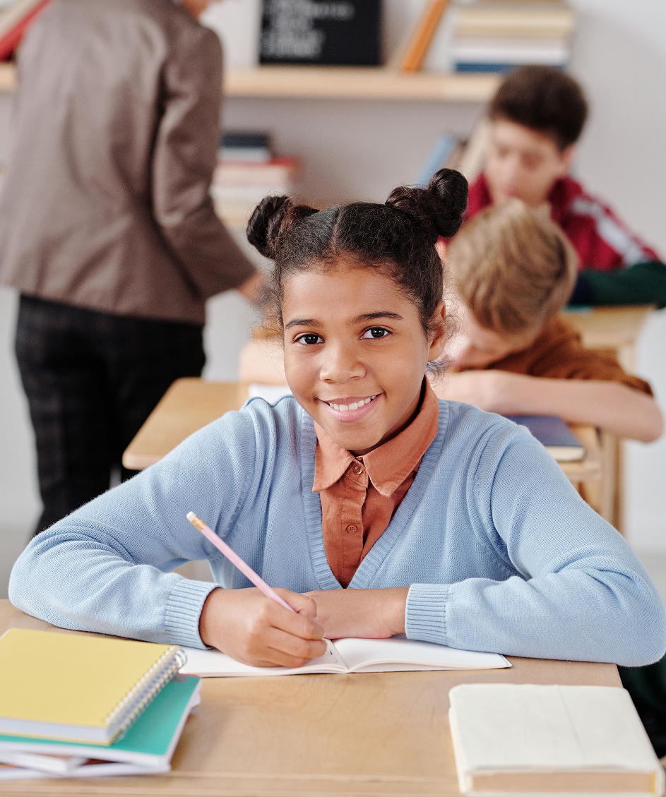 Smiling young girl writing in a notebook at her desk in a classroom, confidently back at school.