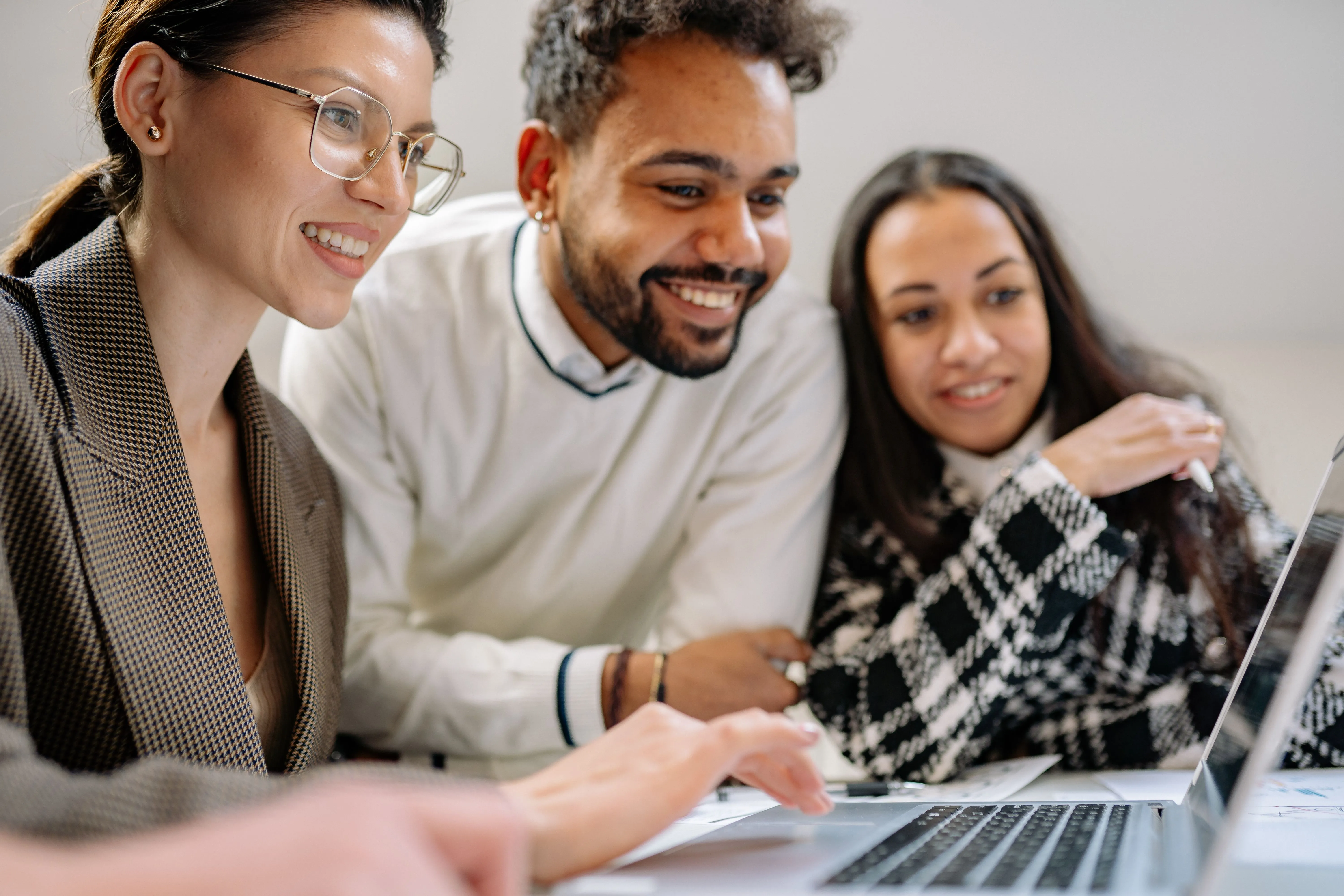 Three smiling people gathered around a laptop, learning together in a supportive community.