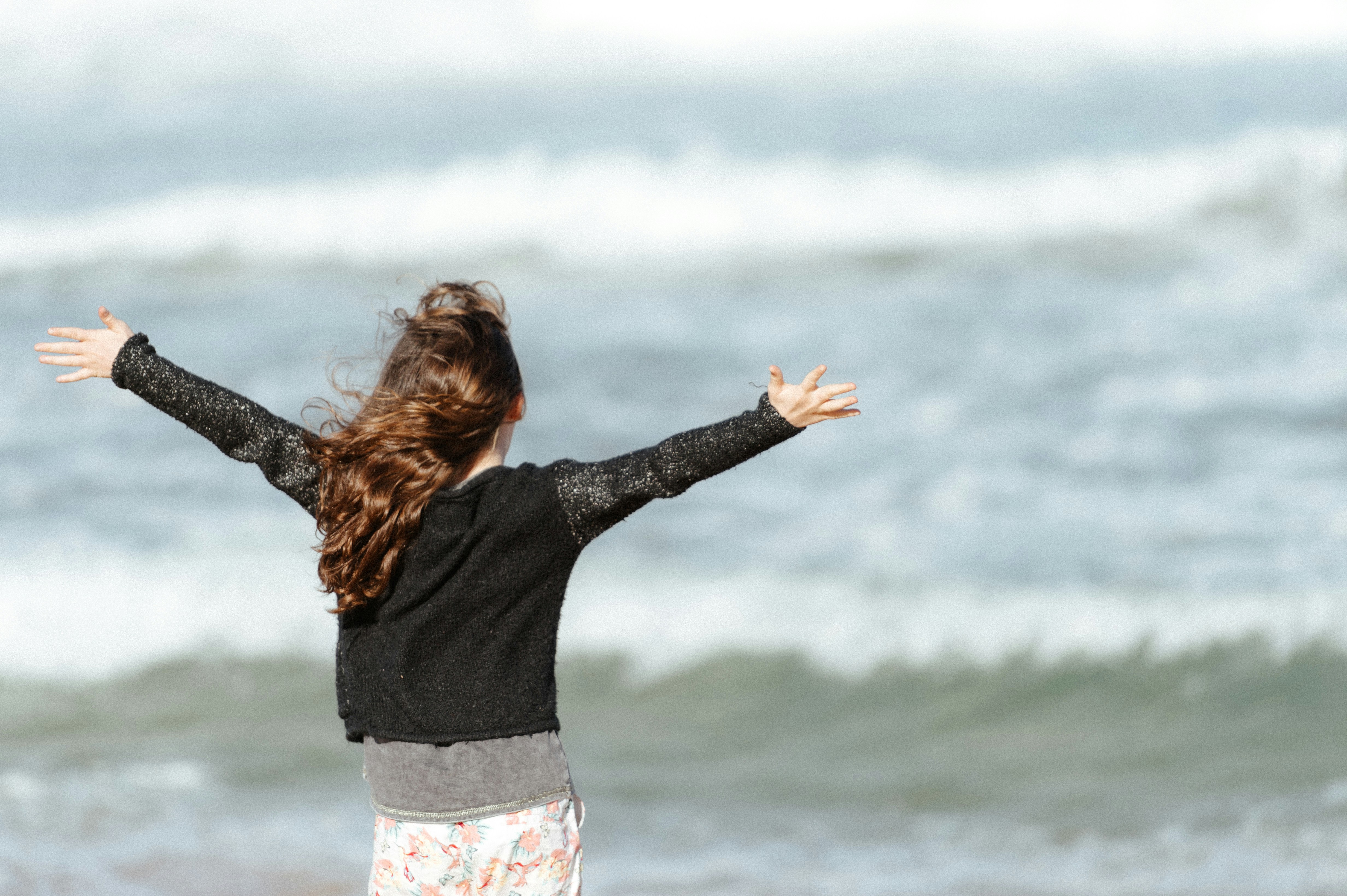 Girl standing on a beach with arms open wide facing the ocean waves, a feeling of freedom and relief.