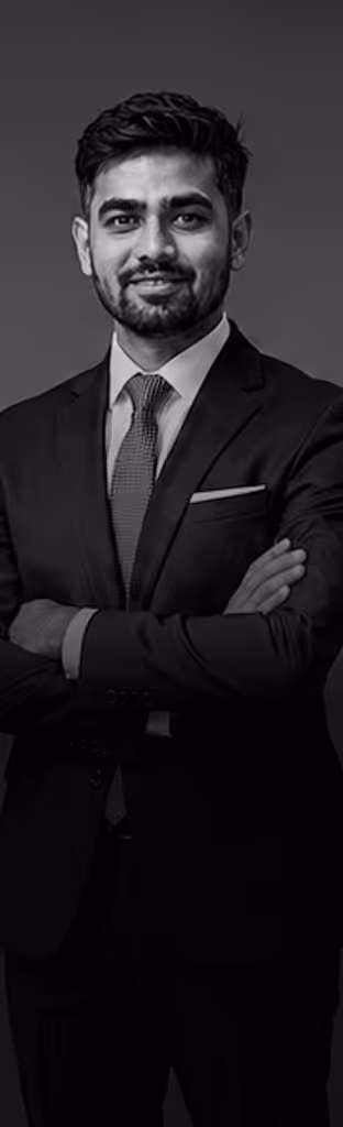 Confident man in a dark suit and tie with arms crossed, smiling and looking at camera.