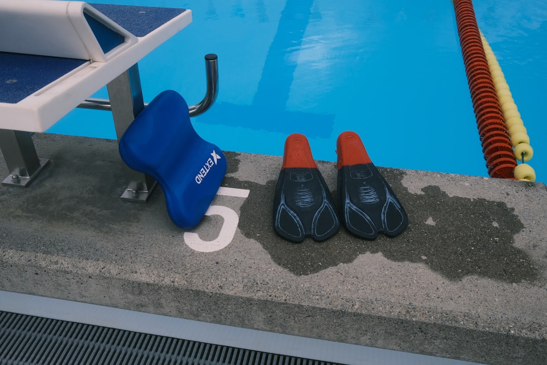 Swimming pool edge with a blue kickboard, black and red swim fins, and a lane divider in water.