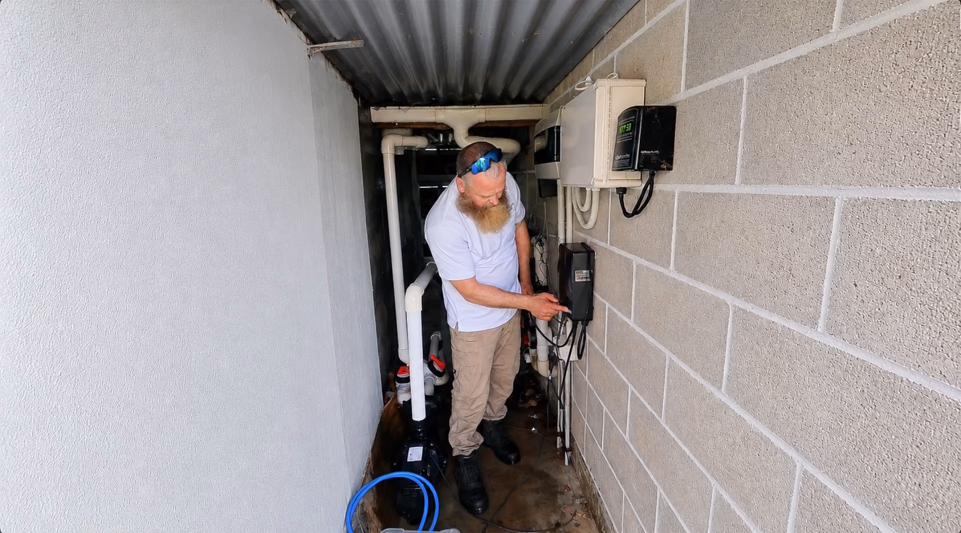 Man with beard and sunglasses adjusting controls on a device mounted on a brick wall.