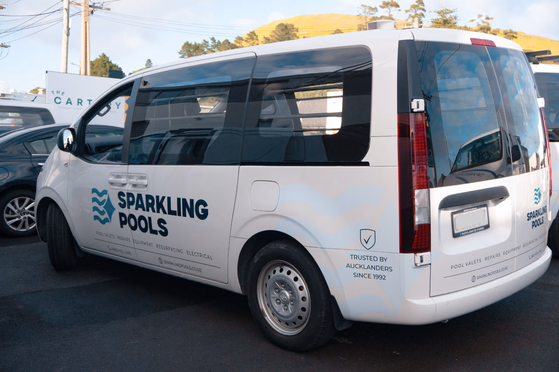 White Sparkling Pools van with blue text and logo parked outside with a hill in the background.