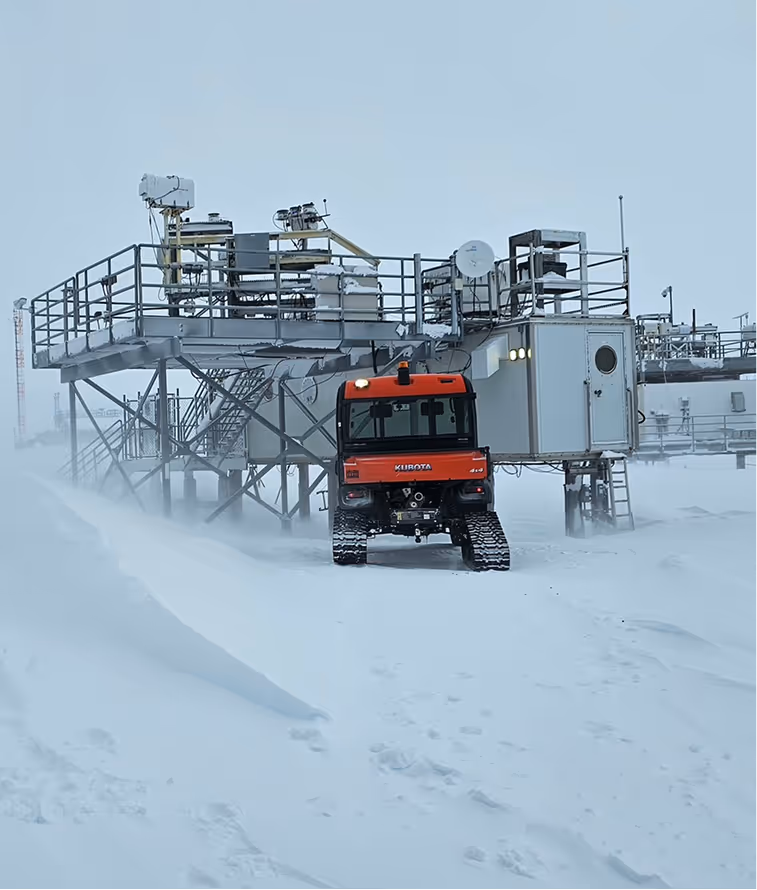 Red tracked vehicle parked outside a raised industrial platform in a snowy, icy landscape.