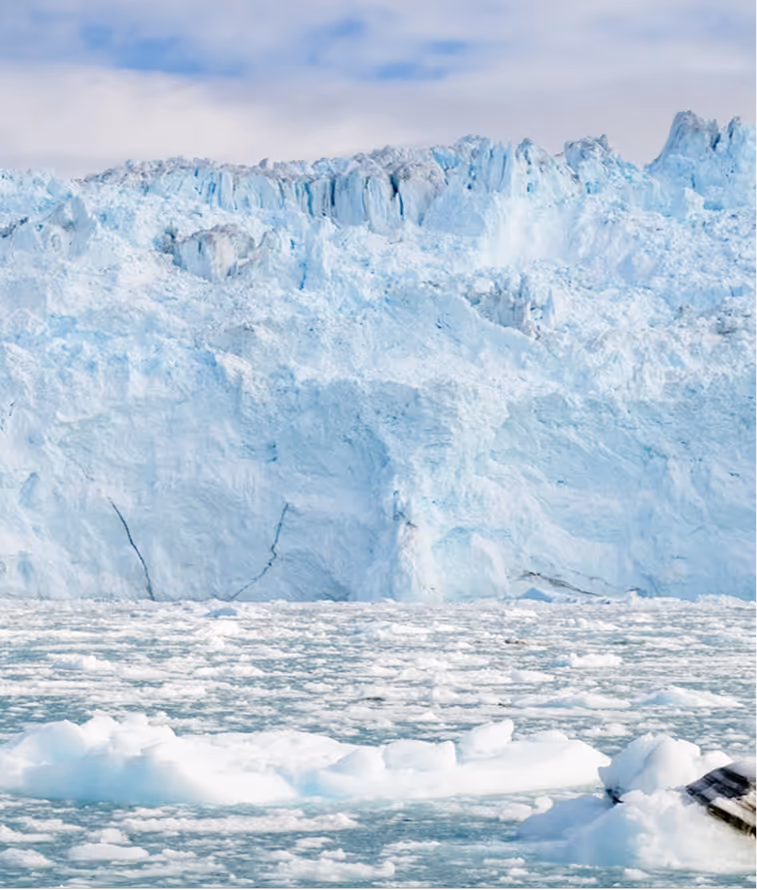 Large glacier with jagged ice formations above icy water with floating ice chunks.