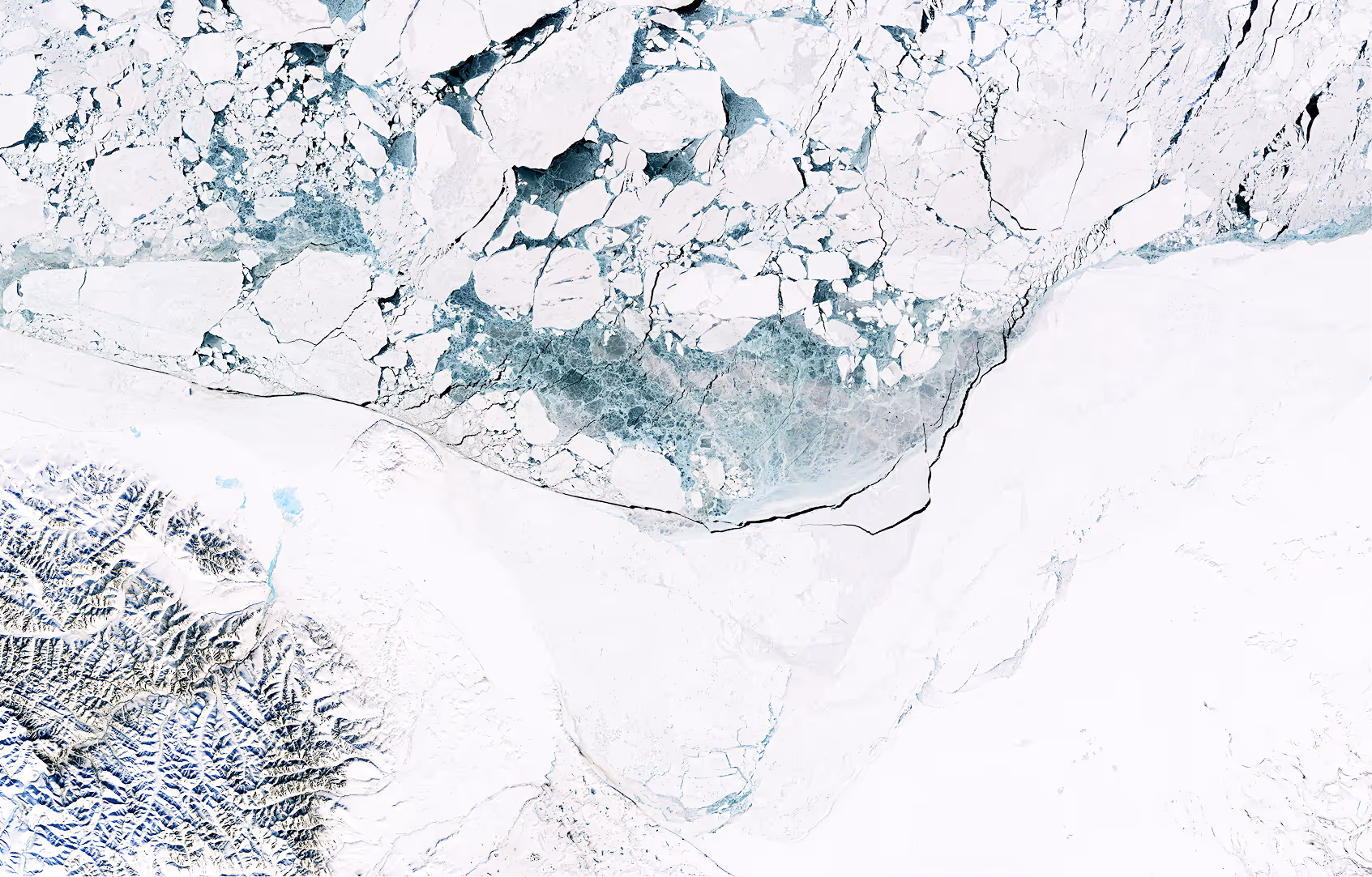 Aerial view of cracked and fragmented ice floating on frigid water over snowy terrain.