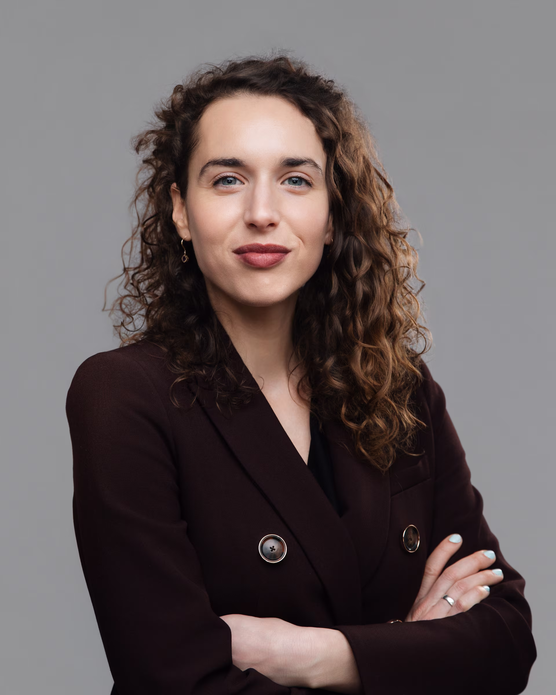 Close-up of a smiling woman with curly hair wearing a black blazer.