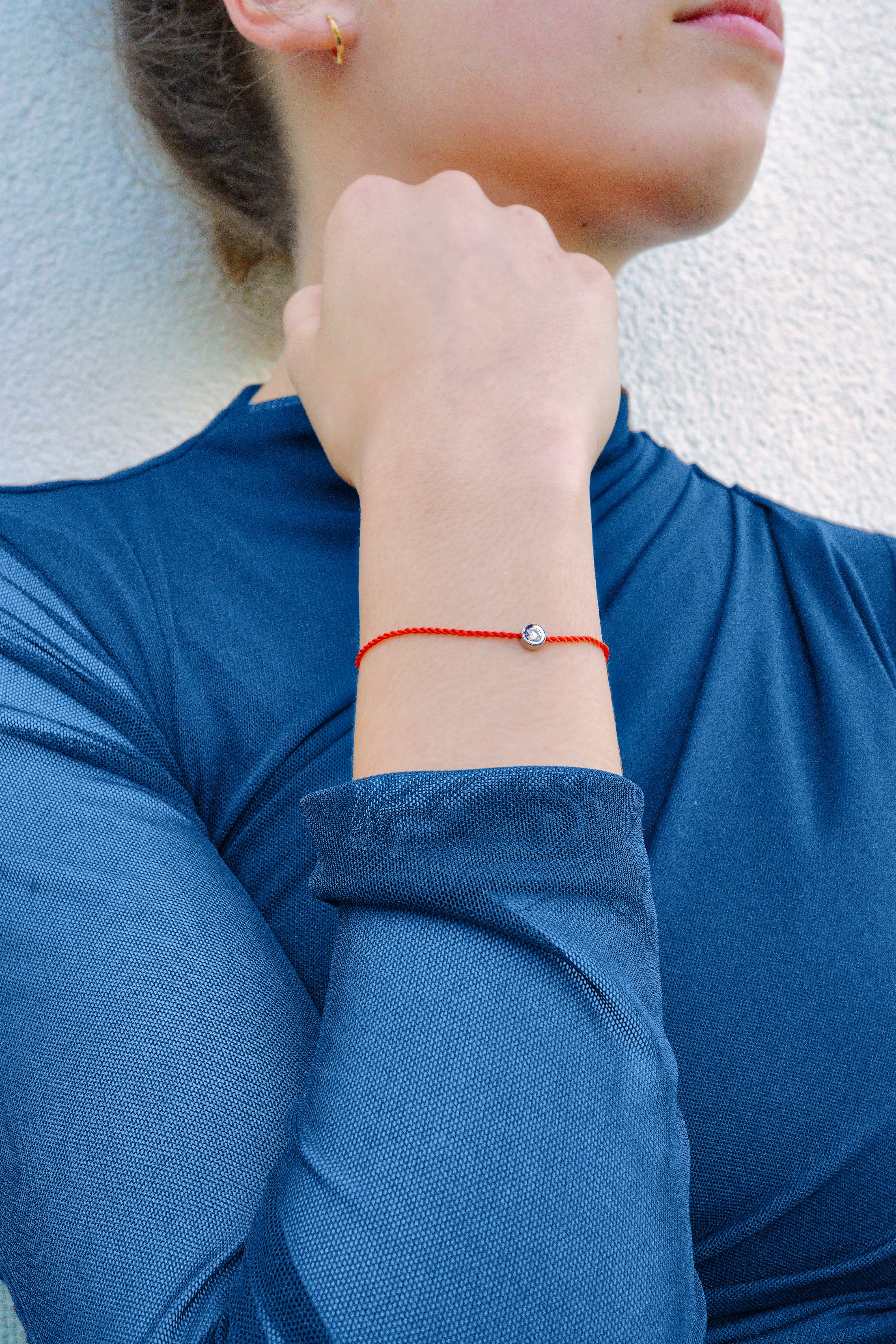 Bracelet ONE porté au poignet, cordon rouge et pierre précieuse, sur tenue sport chic