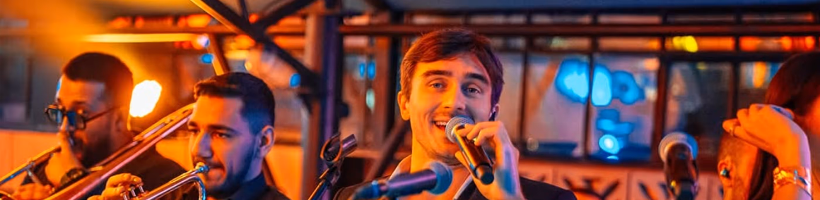Muzičari s puhačkim instrumentima i pevač izvode u osvetljenom klubu.