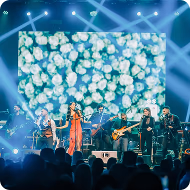 Bend od šest muzičara izvodi nastup na sceni sa velikim ekranom ruža u pozadini.