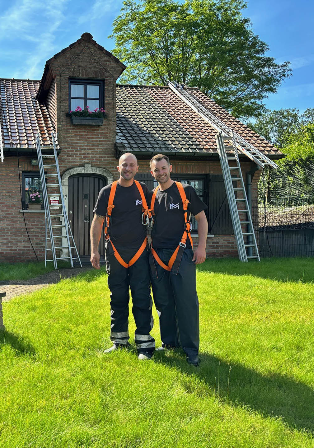 Twee Mossmasters medewerkers met veiligheidsgordels voor een bakstenen woning klaar voor dakreiniging