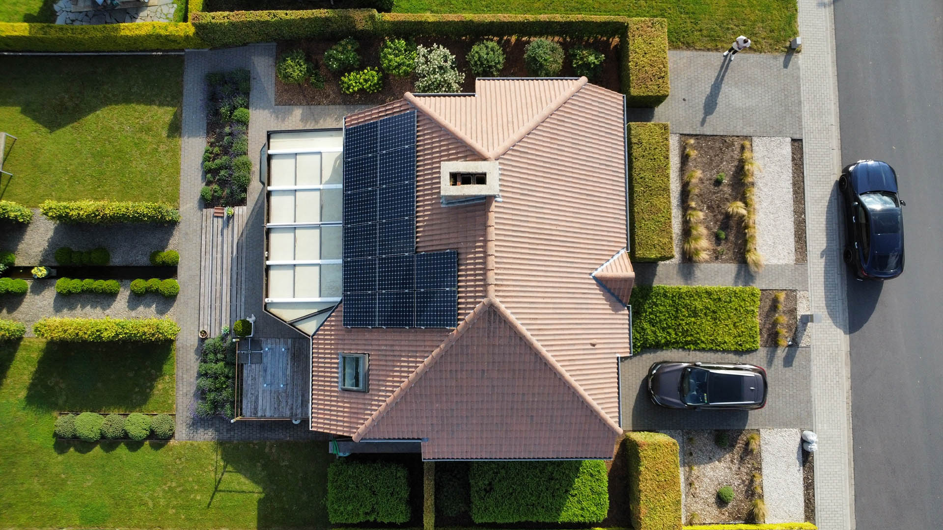 Drone-overzicht van gereinigd pannendak met zonnepanelen en glazen serre bij verzorgde villa na behandeling door Mossmasters