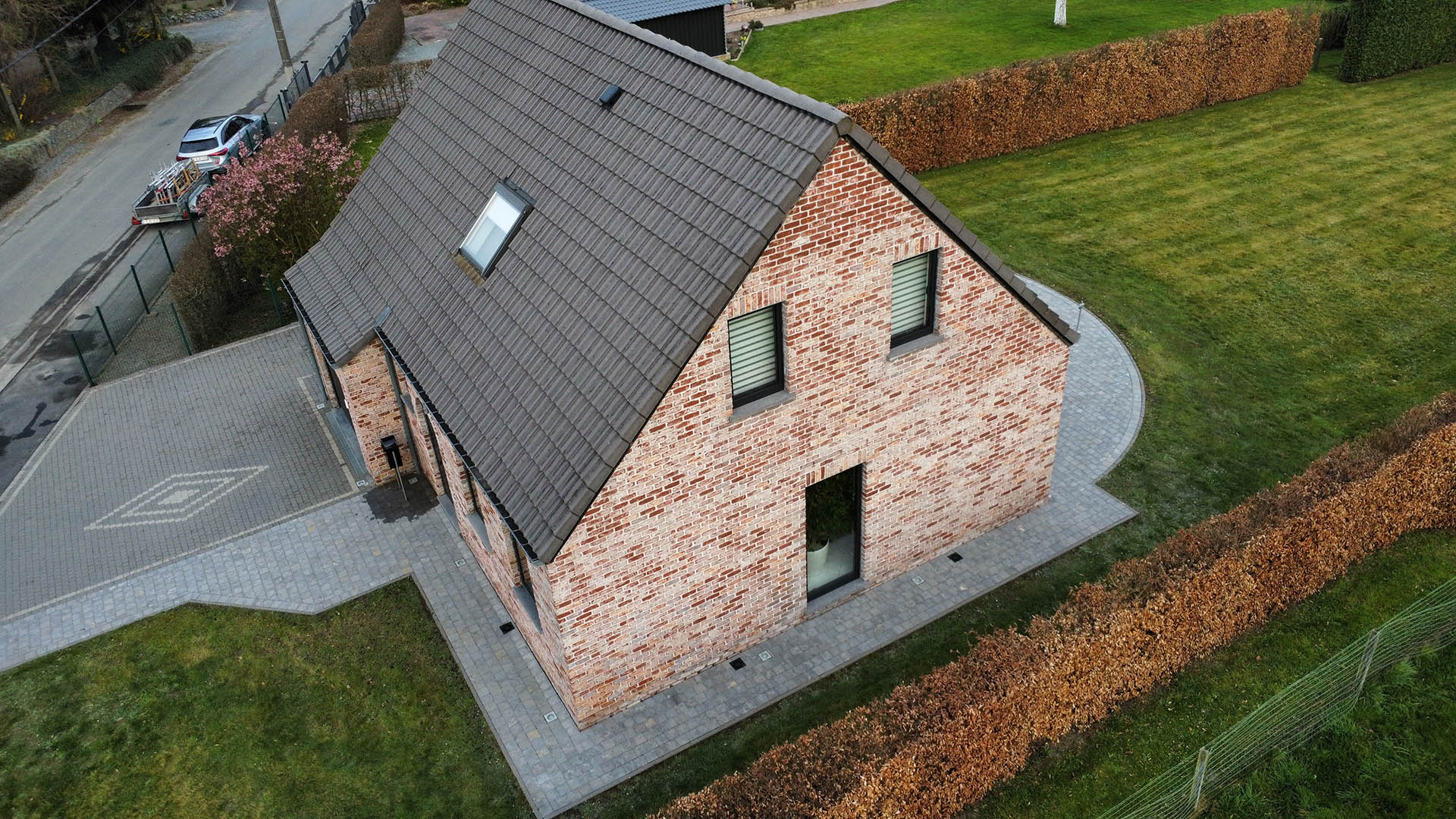 Drone-overzicht van gereinigd donker pannendak en bakstenen gevel van landelijke woning met kasseien oprit door Mossmasters
