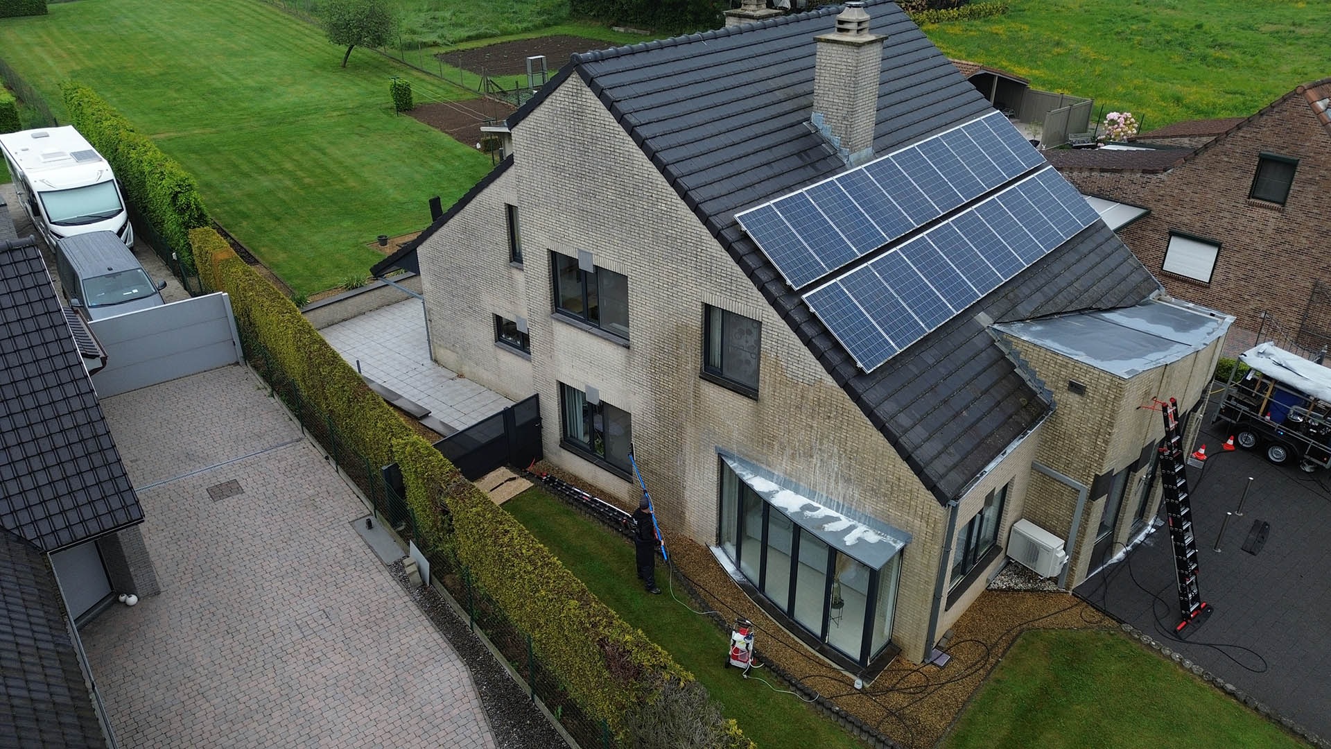Drone-overzicht van woning tijdens gevel en dakreiniging met zonnepanelen door Mossmasters medewerker zichtbaar