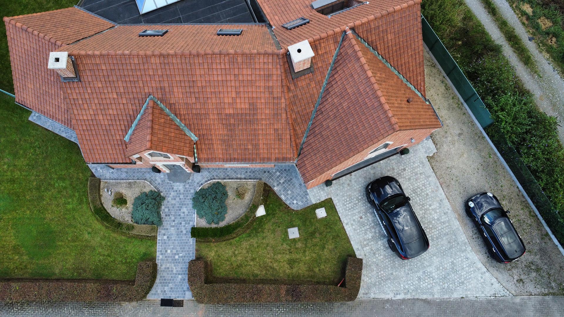 Drone-overzicht van gereinigd pannendak en kasseien oprit bij een woning, behandeling door Mossmasters