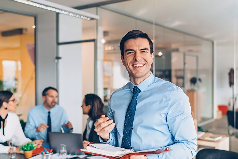 Lächelnder Geschäftsmann im Vordergrund, Team-Meeting im Hintergrund