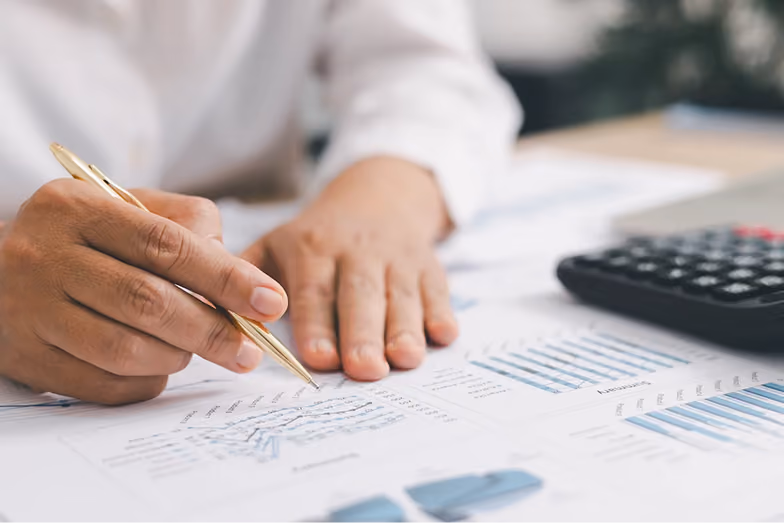 Eine Person analysiert gedruckte Finanzdiagramme mit Taschenrechner am Schreibtisch