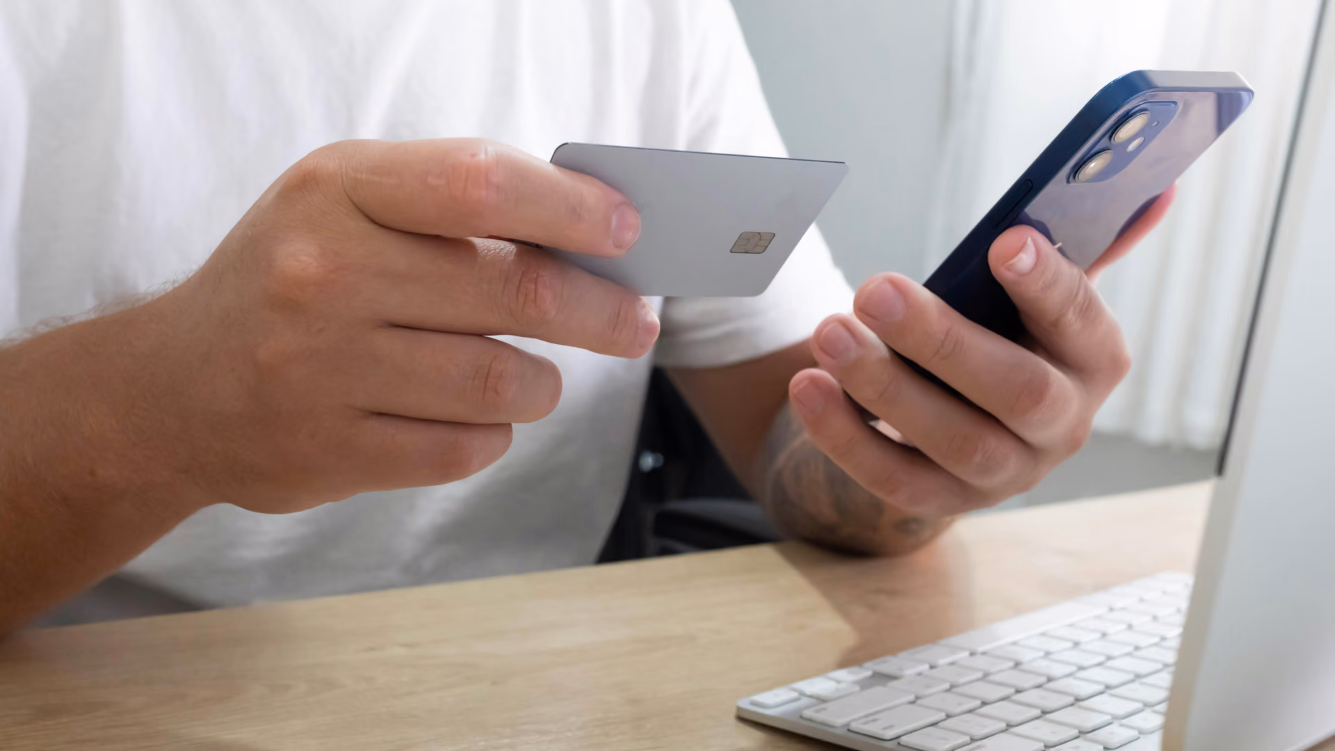 Eine Hand hält ein Handy und die andere hält parallel dazu eine Bankkartee