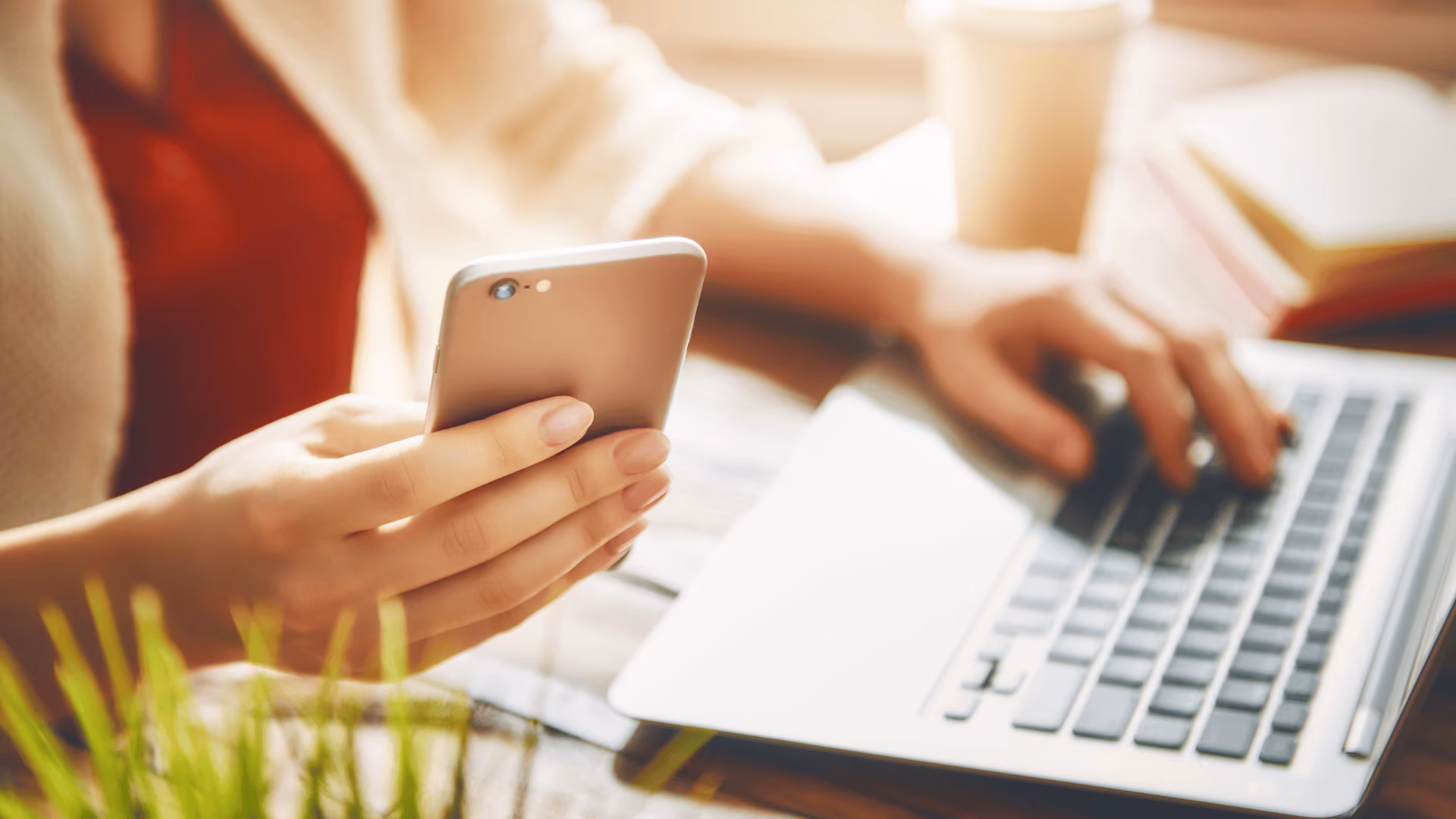 Eine Hand tippt auf der Tastatur eines Laptops, während die andere Hand etwas auf dem Smartphone eingibt a