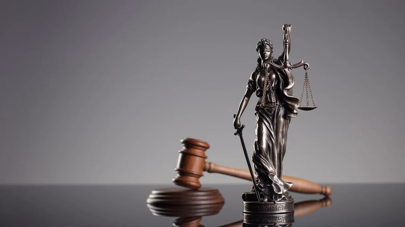 Bronzefigur der Justitia mit Augenbinde, Waage und Schwert neben einem hölzernen Richterhammer