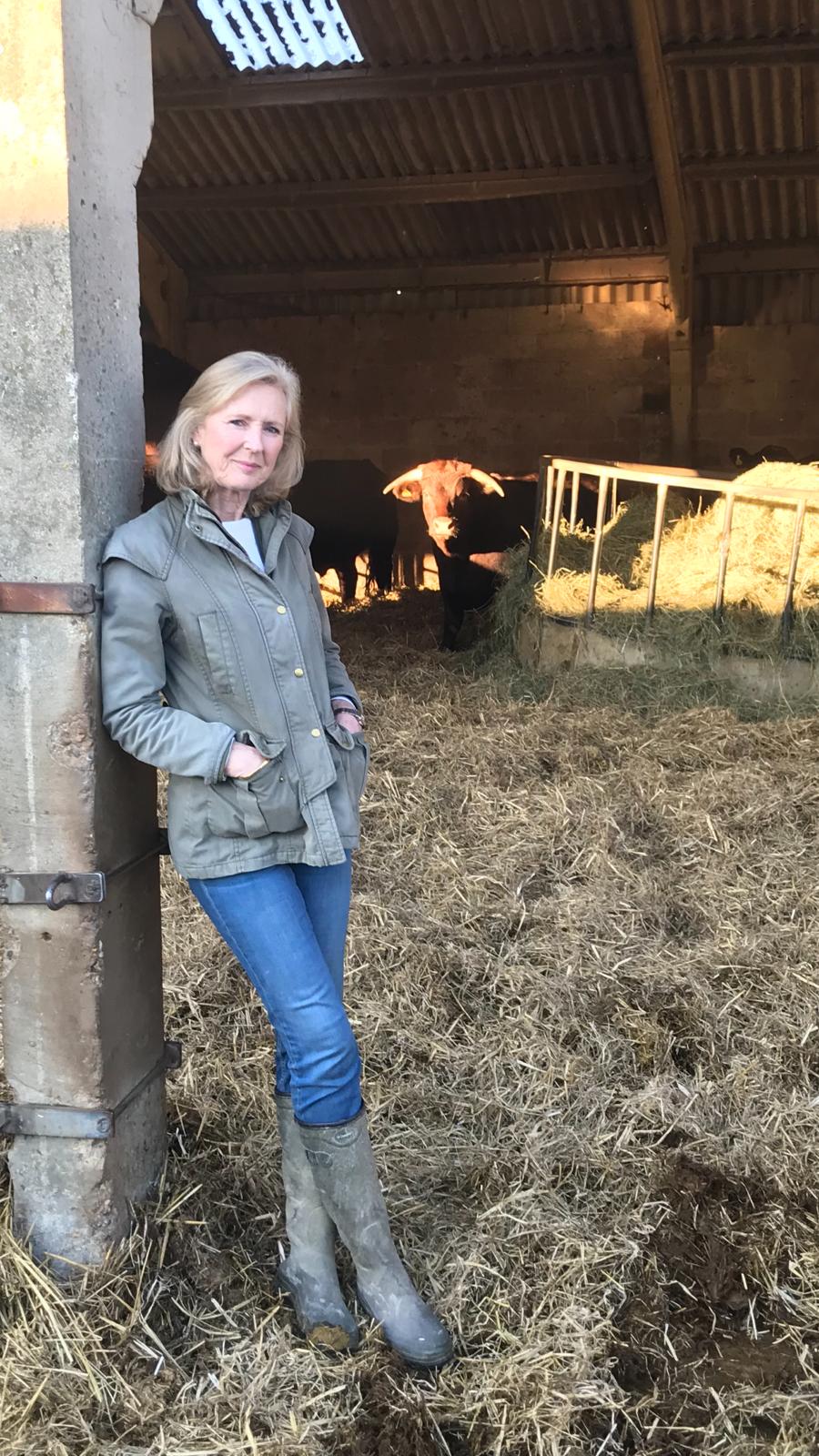 Photo of Carola Godman Irvine leaning on the doorway of a cow shed wearing smart farming clothes and wellington boots