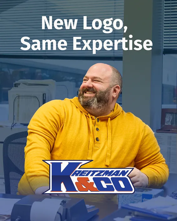 Smiling man in yellow sweater at desk with text New Logo, Same Expertise and Kreitzman K&Co logo.