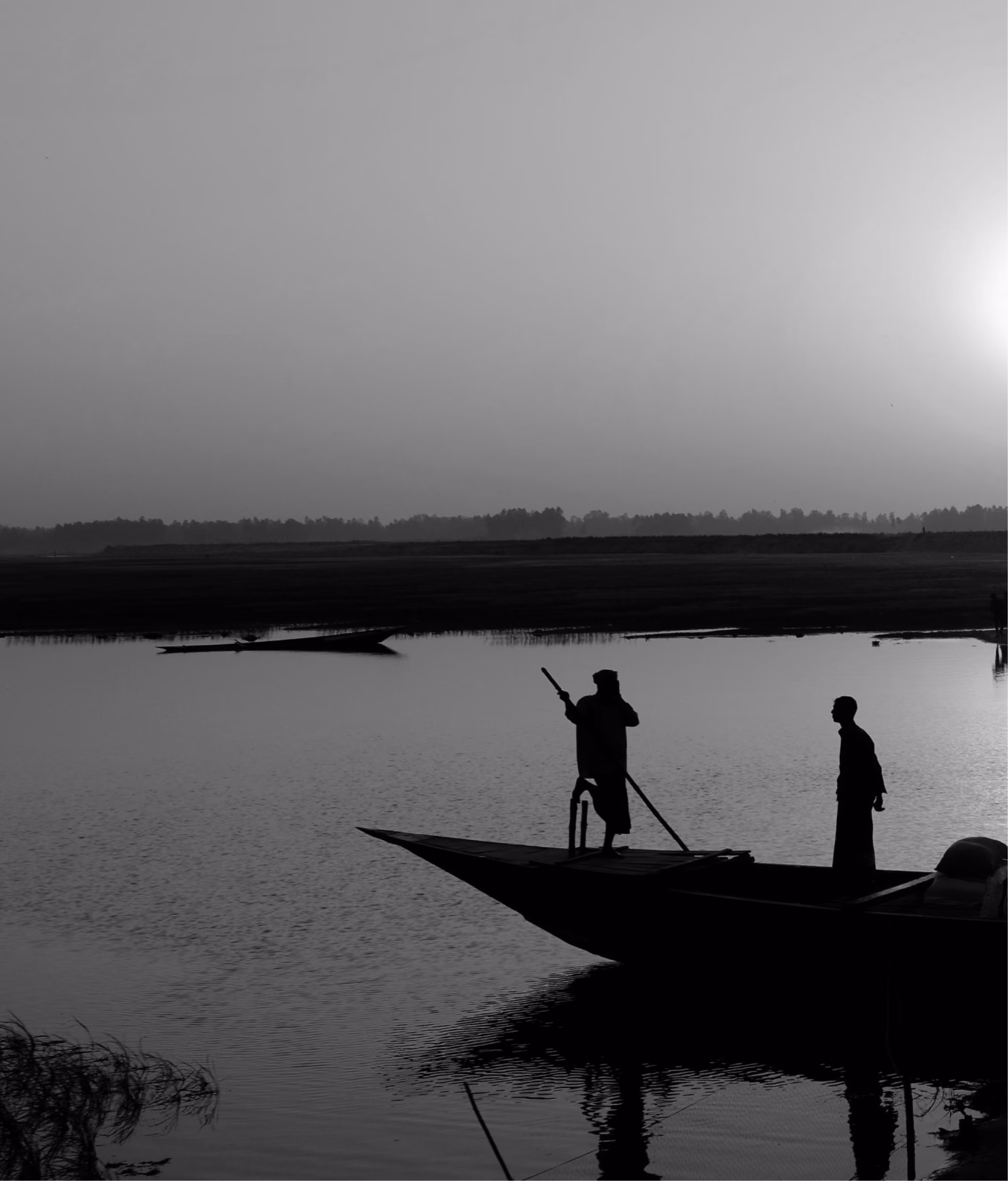 Silhouettes of two people on a boat at sunset on calm water with distant shoreline.