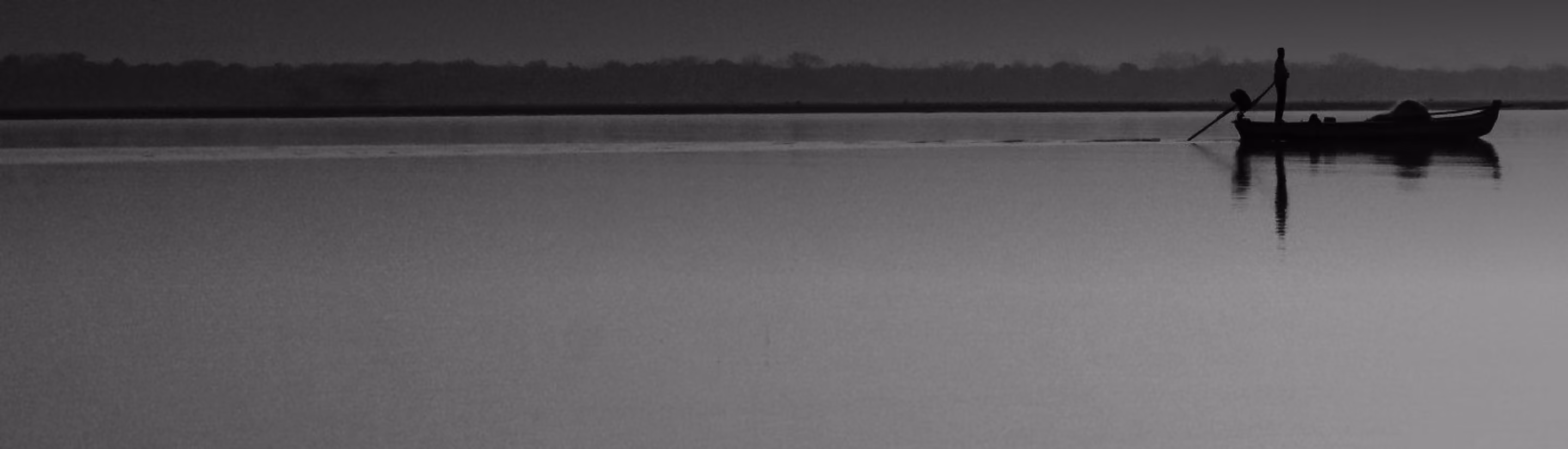 Silhouette of person standing on a boat paddling across calm water at dusk or dawn.
