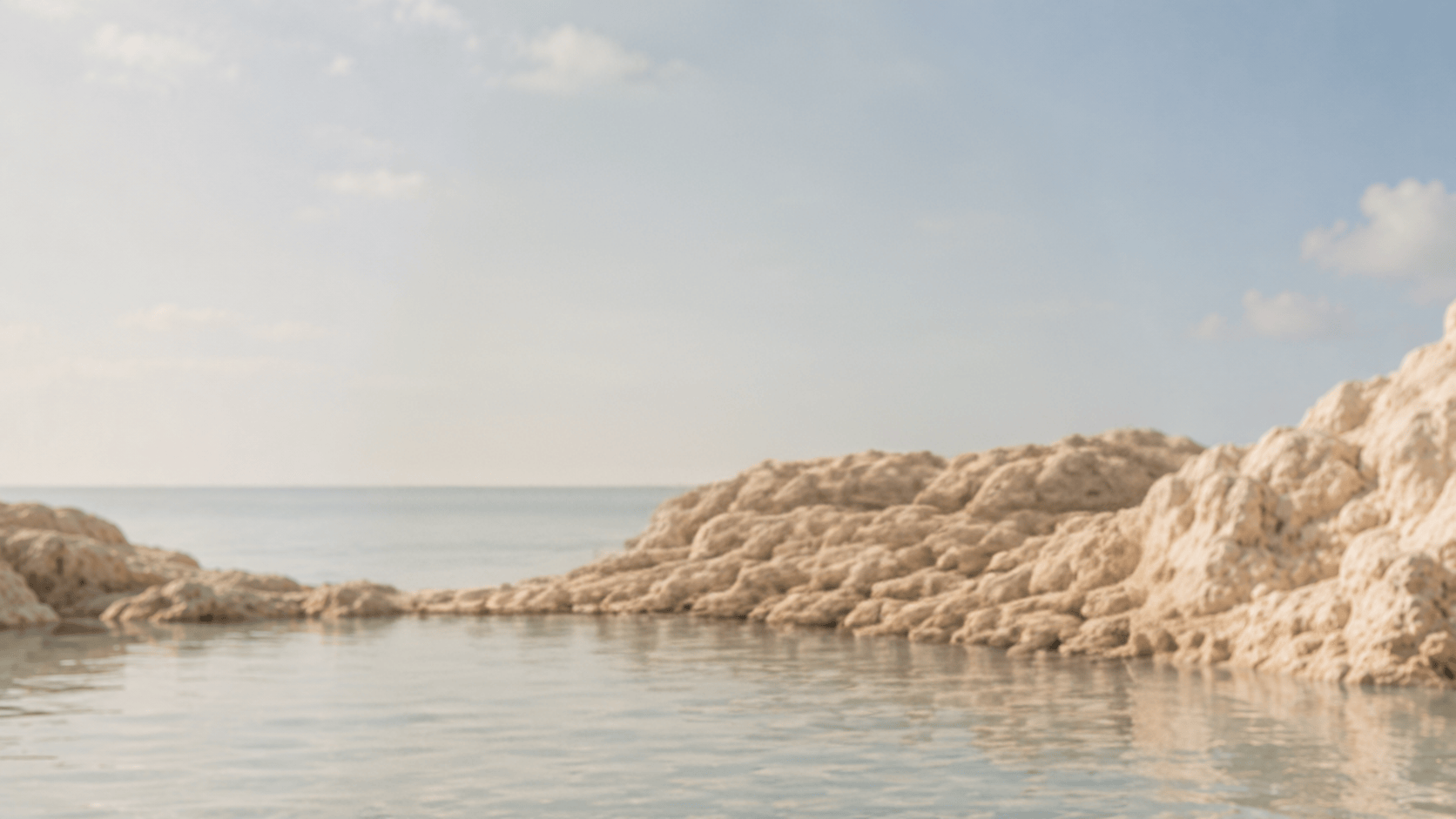 Woman with gold jewelry in brown outfit standing near rocks with ocean and cloudy sky behind her.
