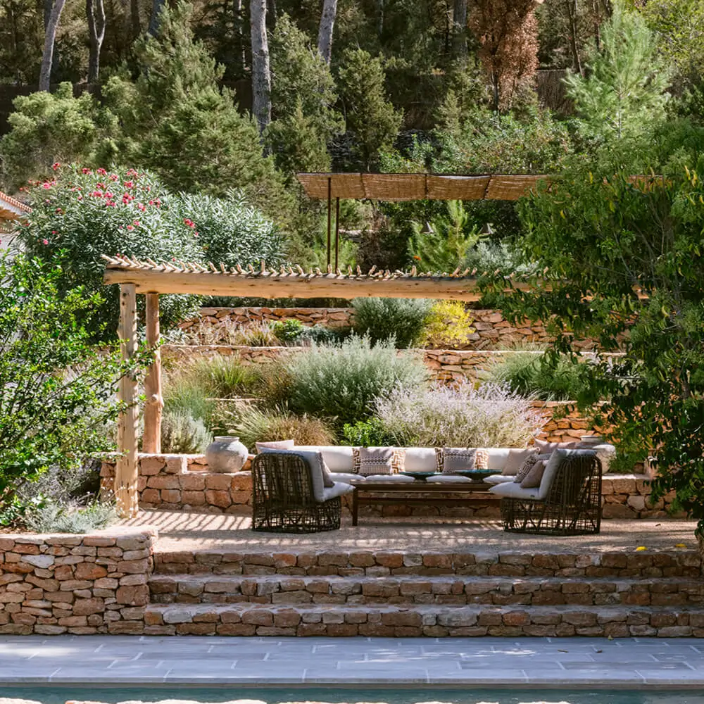 Luxury outdoor lounge and patio design at the Villa Benimussa residential project in Ibiza by Studio Moravová, featuring traditional stone walls and lush Mediterranean landscaping.