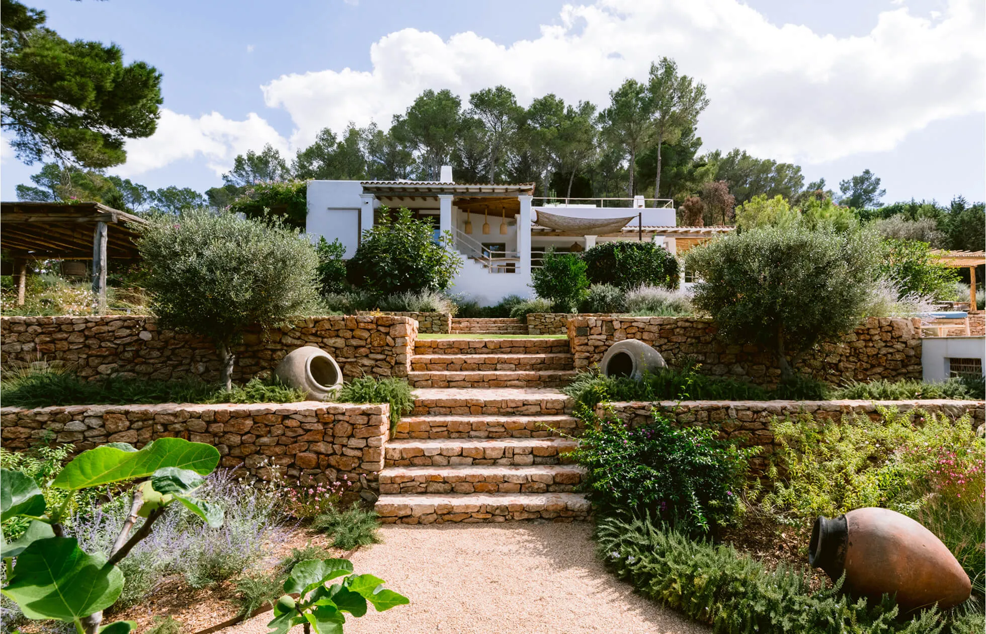 Arquitectura exterior de Villa Benimussa, una lujosa finca mediterránea encalada en Ibiza con paredes de piedra de varios niveles y olivos.