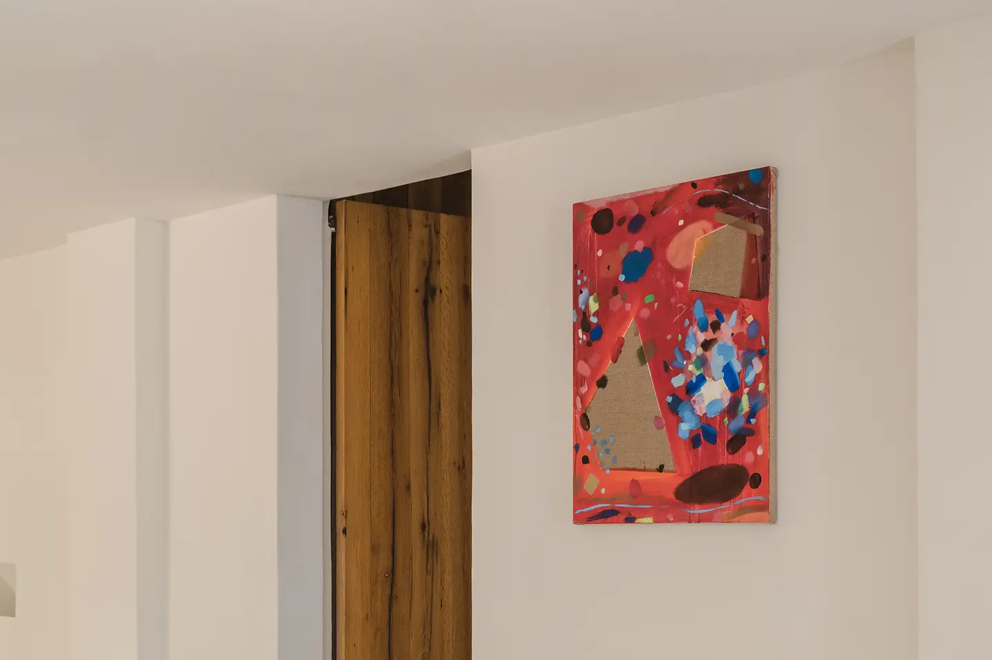 Cuadro abstracto moderno sobre una pared blanca en un espacio minimalista, junto a una puerta de madera rústica. Arte comisariado
